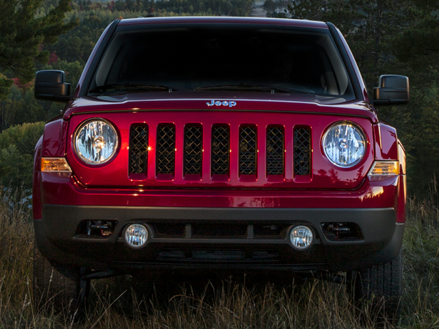 Jeep Patriot SUV with its headlights and fog lights on, parked in tall grass outdoors.