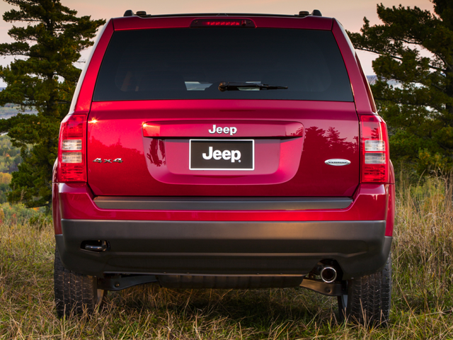 Jeep Patriot SUV on a grassy hillside, with pine trees and hills in the background.