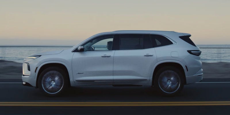SUV driving along a coastal road with the ocean and a pale sky in the background at dusk.