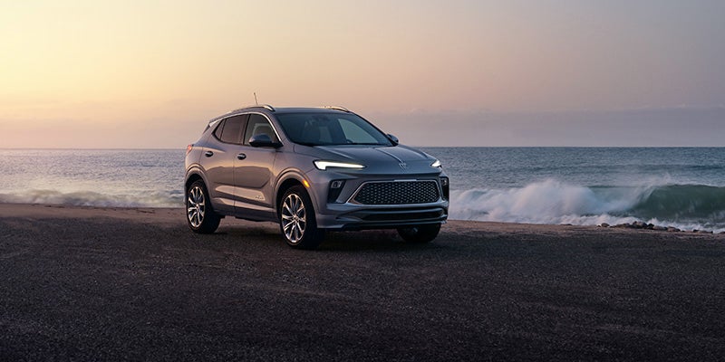 SUV parked on a dark sandy beach with the ocean and waves behind it under a sunset sky.