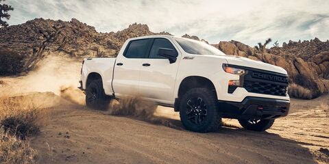 White Chevy Silverado pickup truck kicking up dust while driving off-road through a rocky desert.