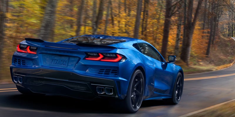 Chevrolet Corvette speeding left on a curved road through autumn trees.