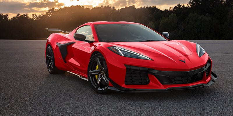 Corvette Z06 supercar with black wheels and yellow brake calipers stands on an asphalt track at sunset.