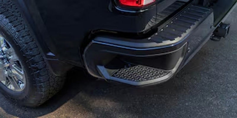Close-up of a black truck's rear bumper, featuring a step with a textured, metallic gray insert.