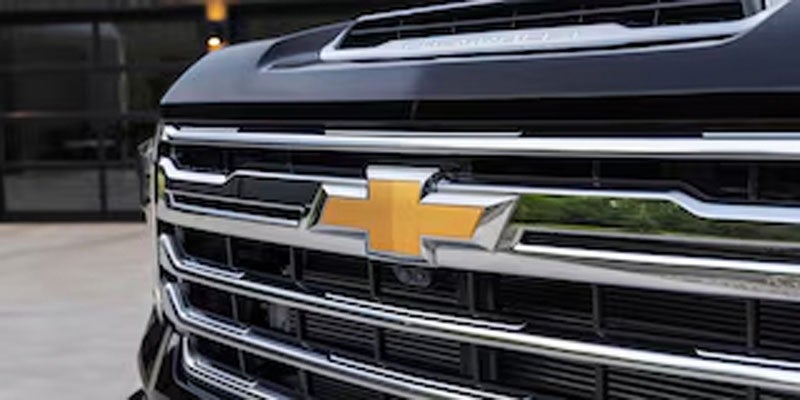 Close-up of a dark Chevrolet truck's front grille with a gold bow-tie logo, chrome trim, and black mesh.