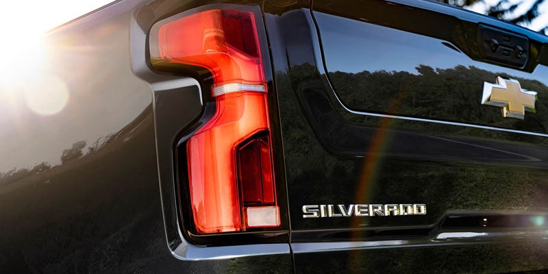 Chevrolet Silverado truck with the taillight illuminated, sun flair in top left.
