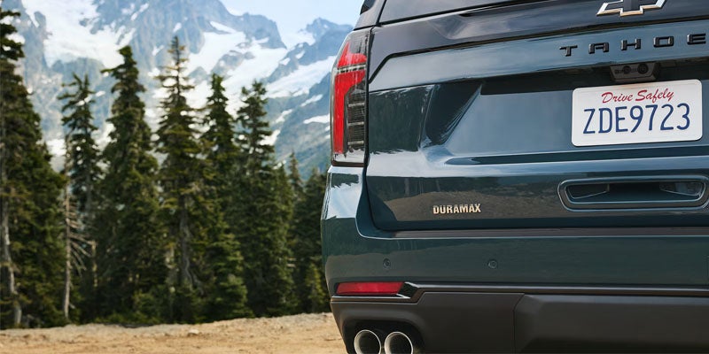 Chevrolet Tahoe parked near pine trees with snowy mountains in the background.