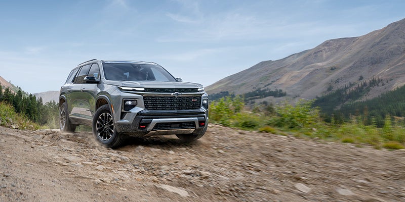 SUV with black wheels driving on a rocky, dirt road in the mountains.