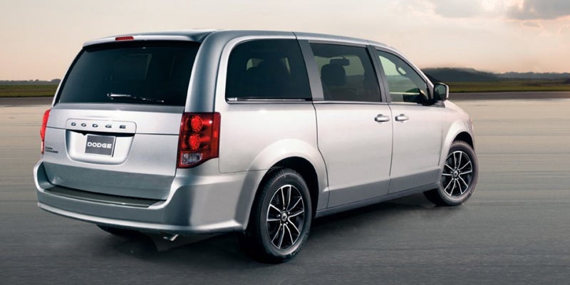 Rear passenger side view of a silver Dodge Grand Caravan parked on a paved surface with a distant skyline.