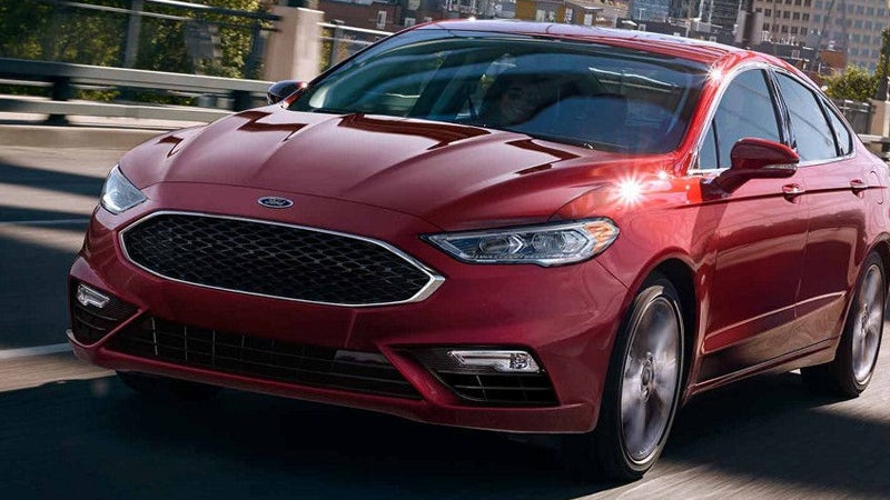 Ford Fusion sedan driving on a city highway, with sunlight glinting off its hood.