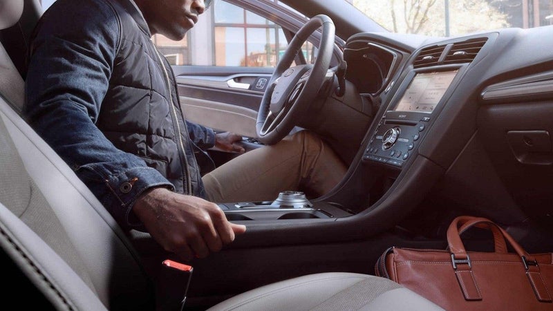 Partial view of a man sitting in the driver's seat of a modern car, with a brown bag on the passenger seat.
