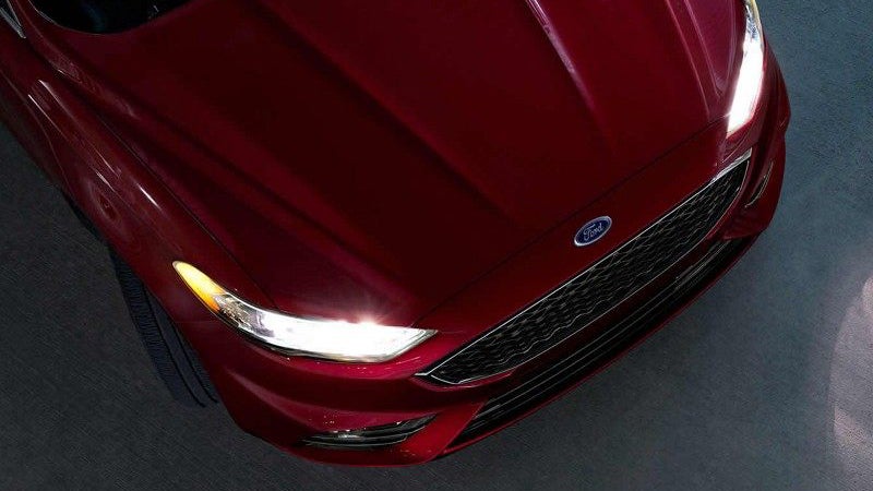 Overhead shot of the front of a glossy cherry red car with its bright headlights on in a dim setting.