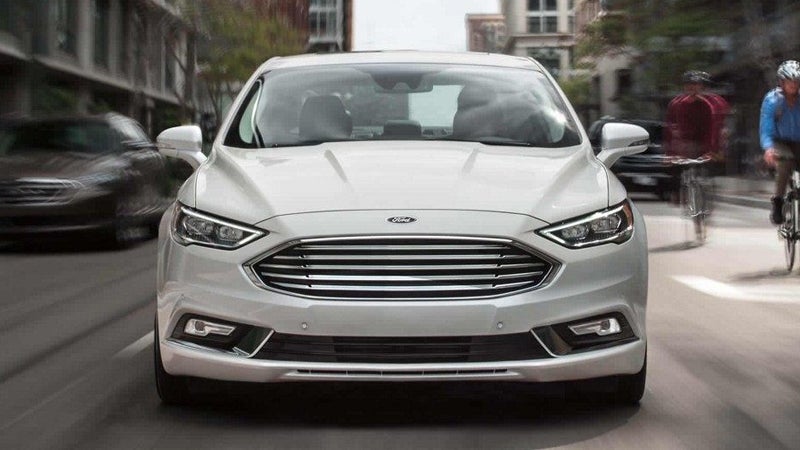 Ford Fusion sedan driving on a city street, with two cyclists in the background.