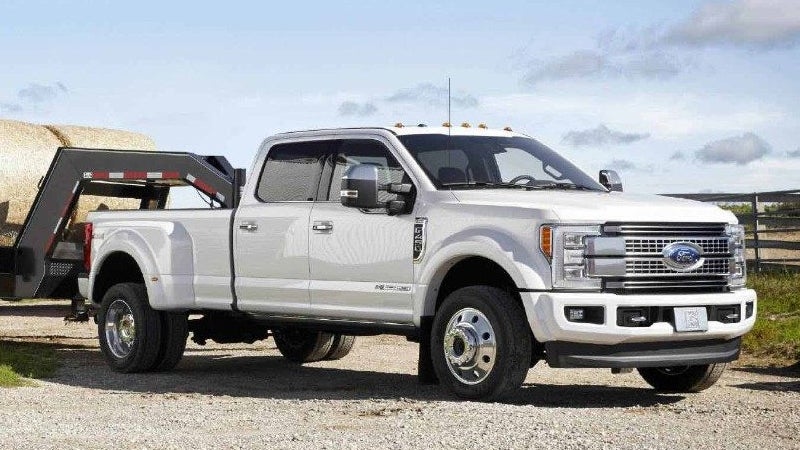 A white Ford F-450 Super Duty pickup truck with a gooseneck trailer carrying hay bales on a gravel road.