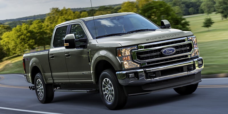 A gray Ford F-250 Super Duty pickup truck driving on a winding paved road through green hills.