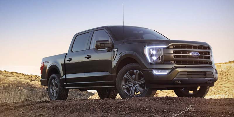 A dark green Ford F-150 King Ranch truck, parked on a dirt incline with its headlights illuminated.