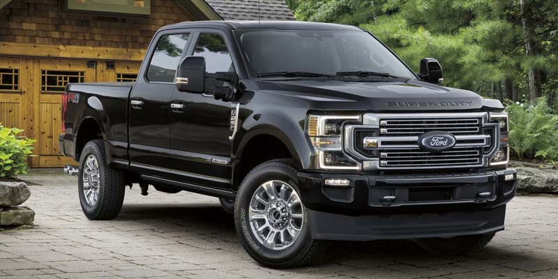 A black Ford F-Series Super Duty truck parked on a paved driveway in front of a rustic wooden house.