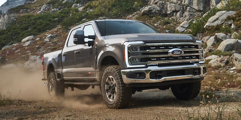 Gray Ford Super Duty pickup truck kicking up dust on a dirt road in a rocky, mountainous landscape.