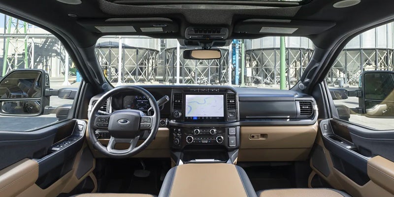 Interior view of a modern truck cabin with a dashboard, steering wheel, large GPS screen, and industrial background.