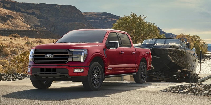 A red Ford F-150 pickup truck is backed up to a boat launch, ready to launch a black speedboat.