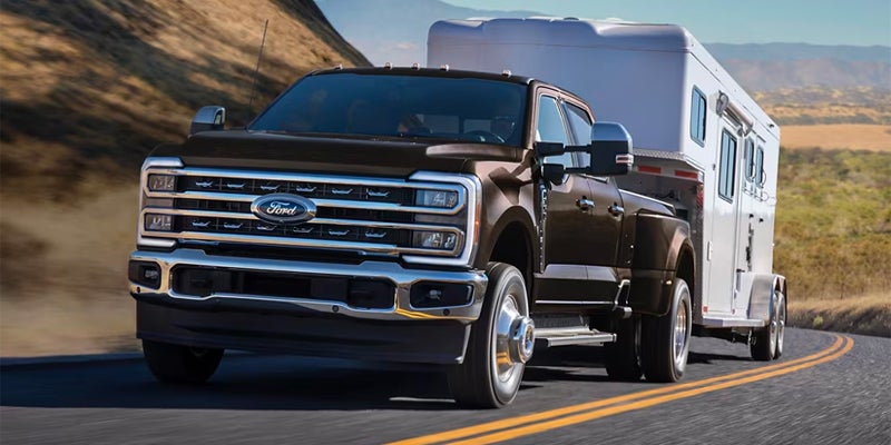 Ford Super Duty dually truck driving on a curved road, towing a white horse trailer.