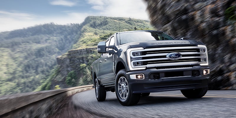 Ford Super Duty truck drives around a curve on a mountain road with a blurry green landscape.