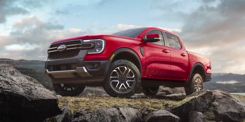 Red Ford Ranger pickup truck with a black grille and silver accents, parked on a rocky cliff overlooking a landscape.