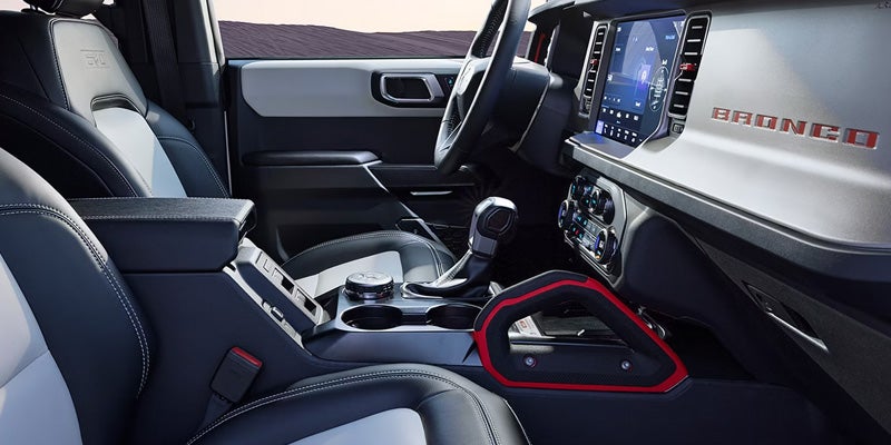The interior of a Ford Bronco features a modern dashboard with a large touchscreen and red trim accents.