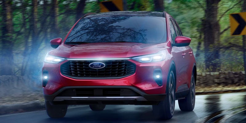 Ford SUV driving on a wet road in a forest, with its headlights on and a glowing light bar across the grille.