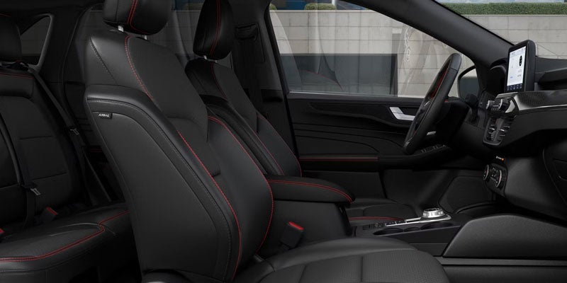 Interior view of a car with black leather seats, red stitching, touchscreen display, and a modern dashboard.