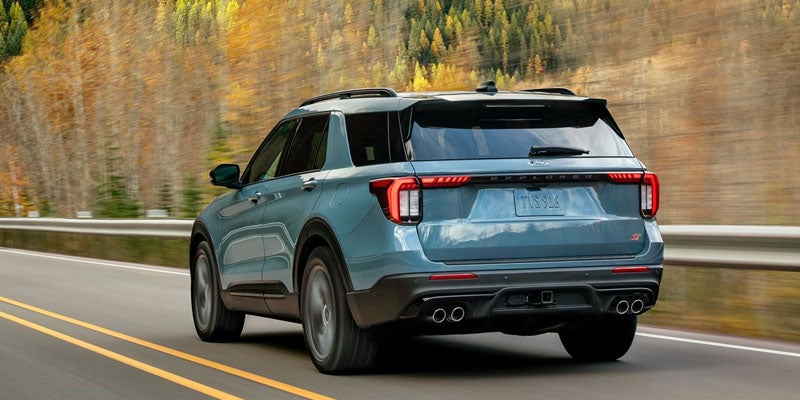 Ford Explorer ST driving on a two-lane road flanked by autumn trees.