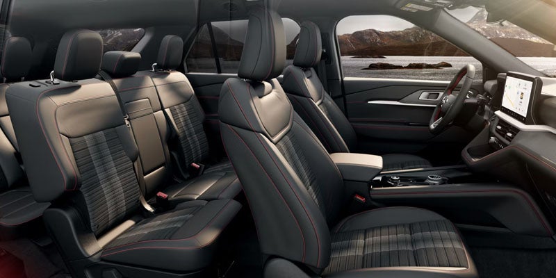 Interior of a three-row SUV showing black seats with red stitching and plaid inserts, and a steering wheel.