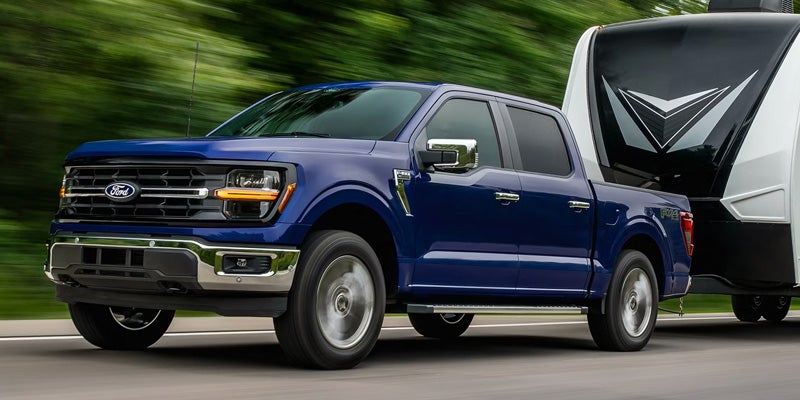 A blue Ford F-150 pickup truck towing a black and white travel trailer on a highway.