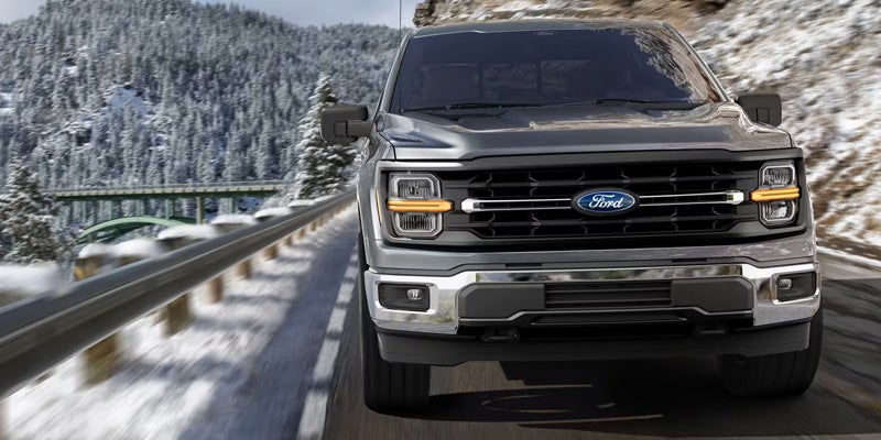 Front view of a dark gray Ford F-150 pickup truck driving on a snowy mountain road