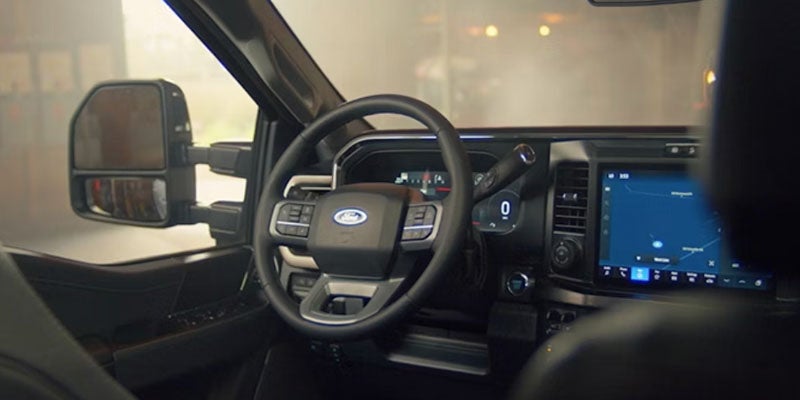 Interior shot of a modern car showing the steering wheel with Ford logo, digital dashboard, and navigation screen.