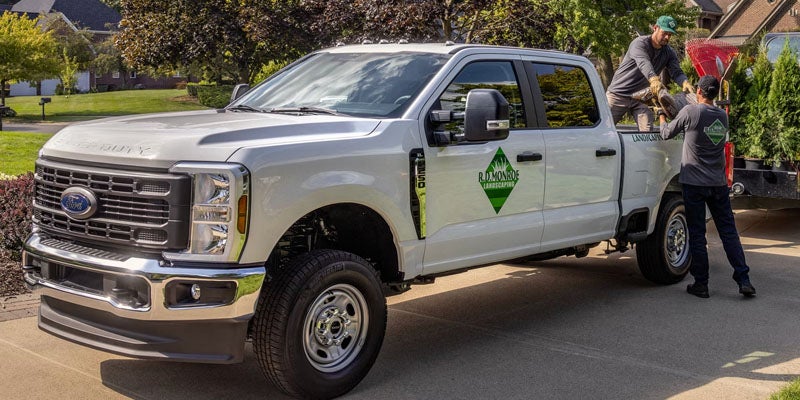 White R.D. Monroe Landscaping truck with two landscapers loading plants in the back.