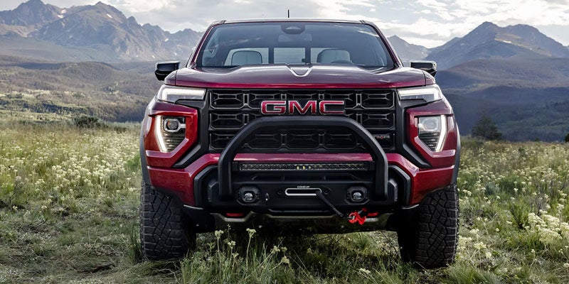 Front view of a red GMC Canyon pickup truck with a winch and roll bar, in a field with mountains.