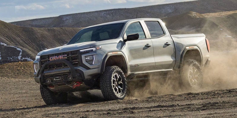 A gray GMC Canyon truck kicks up dust as it drives over rough terrain.