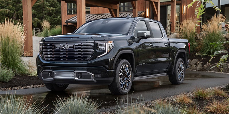 Black GMC pickup truck parked outside a modern home with landscaped surroundings.