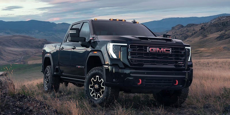 A dark gray GMC Sierra AT4X heavy-duty truck parked on a grassy hillside overlooking a mountain valley.
