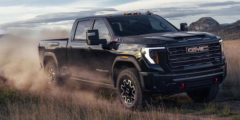 A black GMC truck drives through a field, kicking up dust as it travels.