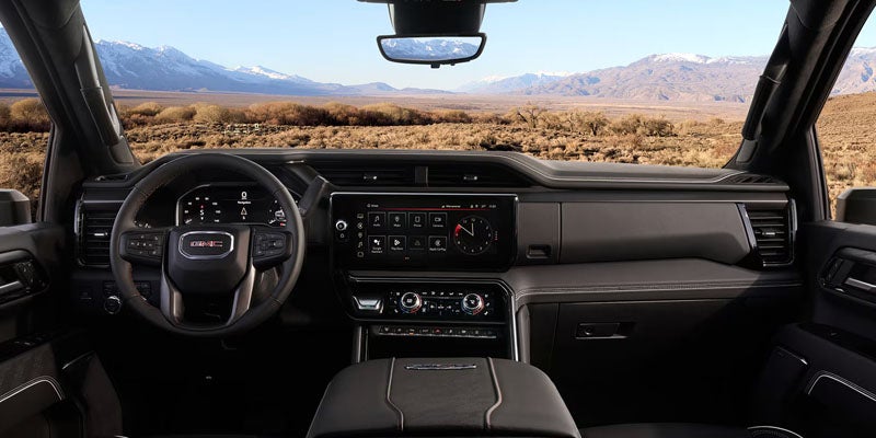 The interior of a dark GMC truck faces a snowy mountain range and desert landscape.
