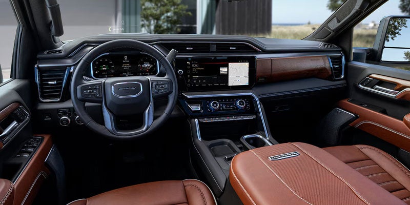 Driver's perspective of a luxury vehicle interior with tan leather, wood trim, large infotainment screen, and steering wheel.