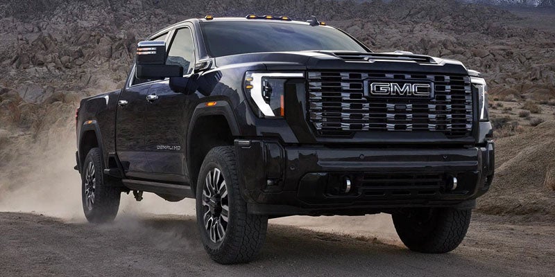 A black GMC Denali HD pickup truck on a dirt road, with dust kicking up from its tires.