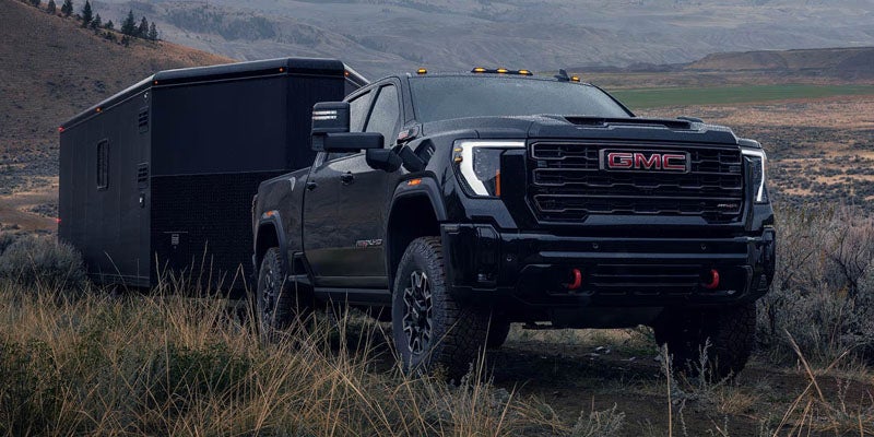 A black GMC pickup truck with a trailer stands in a grassy field under a cloudy sky.