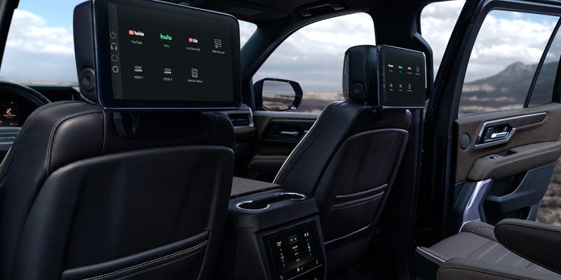 Rear interior of a modern SUV showing two dark screens and dark leather seats.