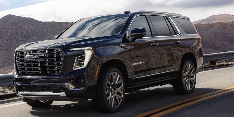GMC Yukon Denali SUV on a winding road with mountains in the background.