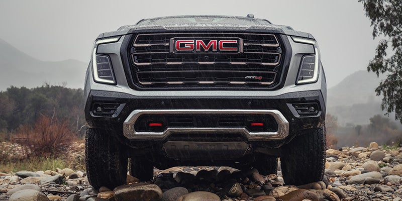 GMC Canyon AT4X pickup truck on a rocky terrain with wet surfaces and mountainous backdrop.