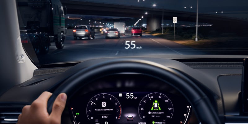 A driver's view from inside a car at night, showing a heads-up display projecting '55 mph' onto the road.