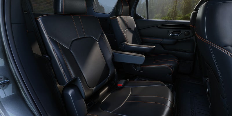 Dark gray leather captain's chairs with orange stitching in the second row of an SUV.